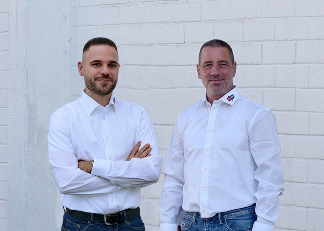 Yannik Kopp und Andreas Kersken stehen im weißen Hemd vor einer weißen Mauer